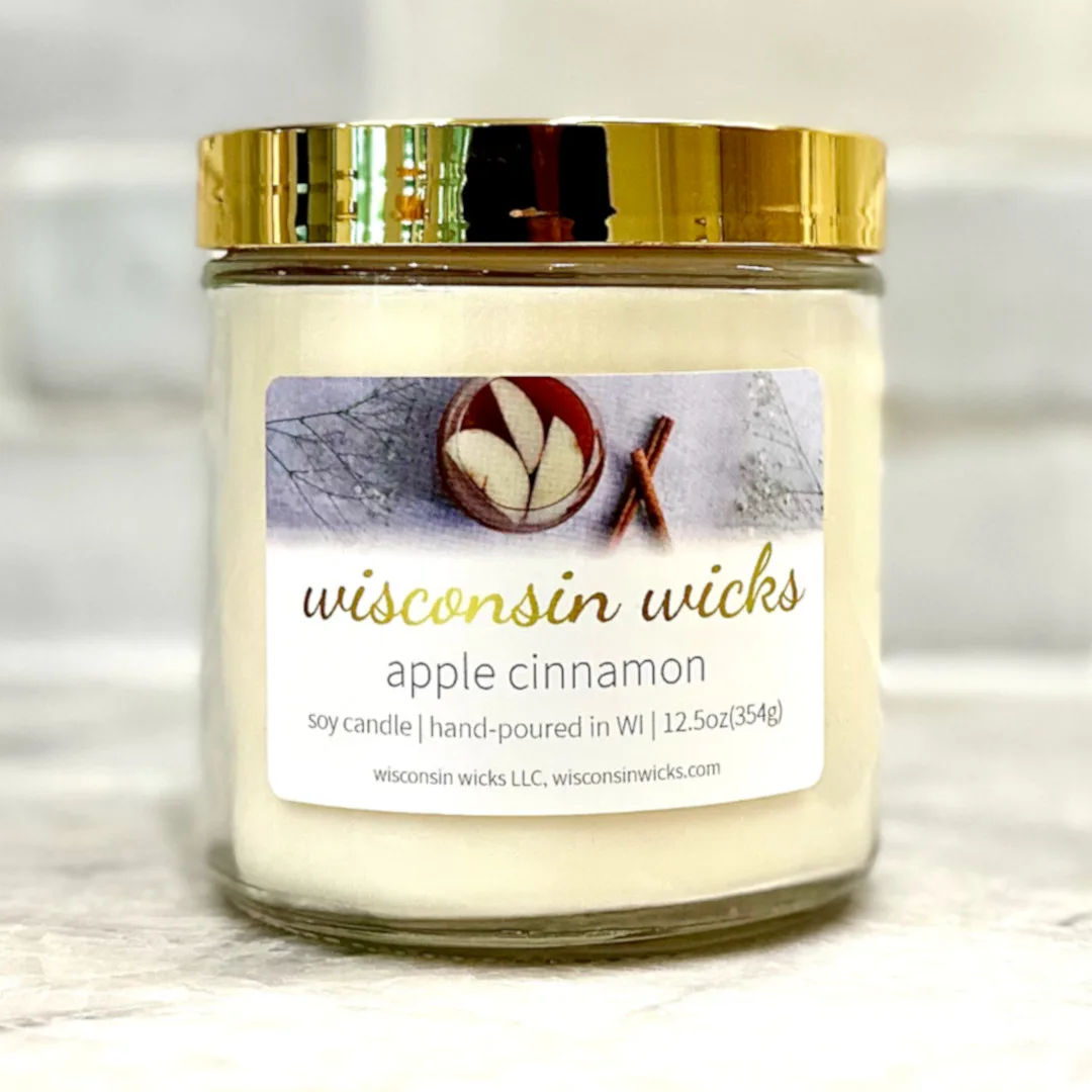 Elegant gold candle adorned with a label featuring visuals of apple slices and cinnamon sticks displayed on marble countertop
