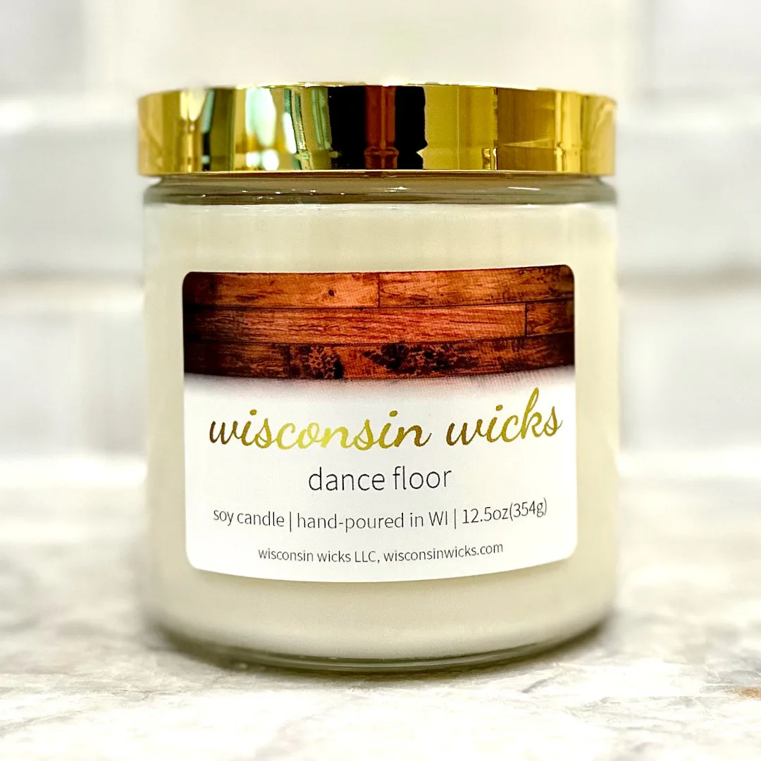 Lavish gold candle adorned with a label featuring visuals of a footprint-laden wooden dance floor displayed on marble countertop