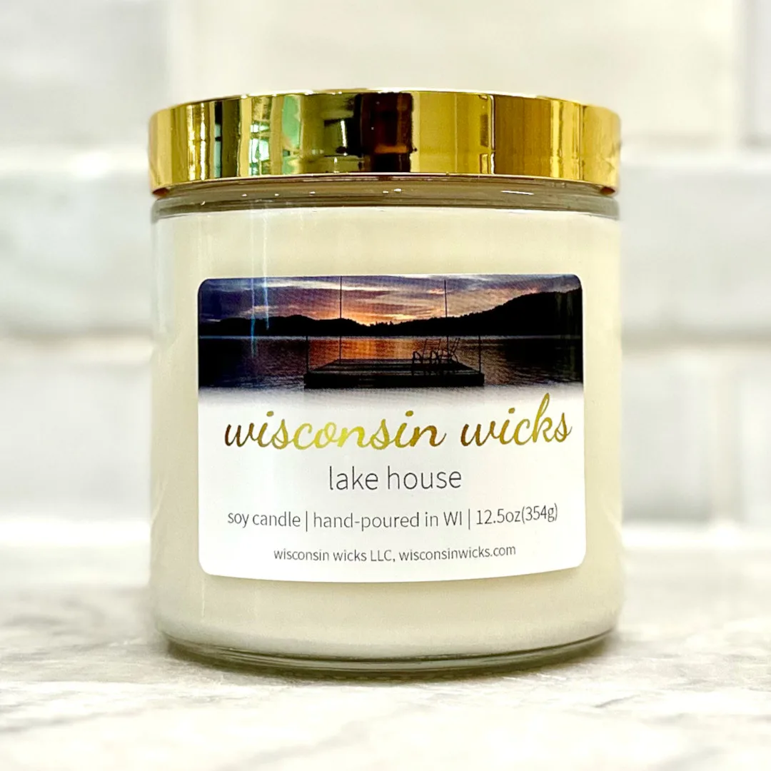 Opulent gold candle adorned with a label featuring visuals of a peaceful sunset near a dock overlooking a lake displayed on marble countertop