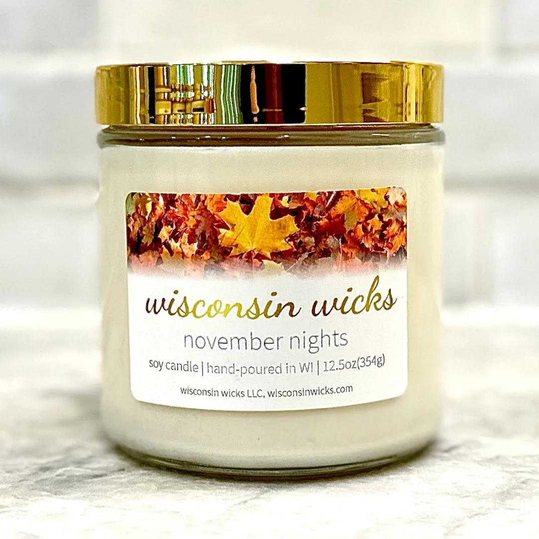 Elegant gold candle adorned with a label featuring visuals of fallen maple leaves displayed on marble countertop
