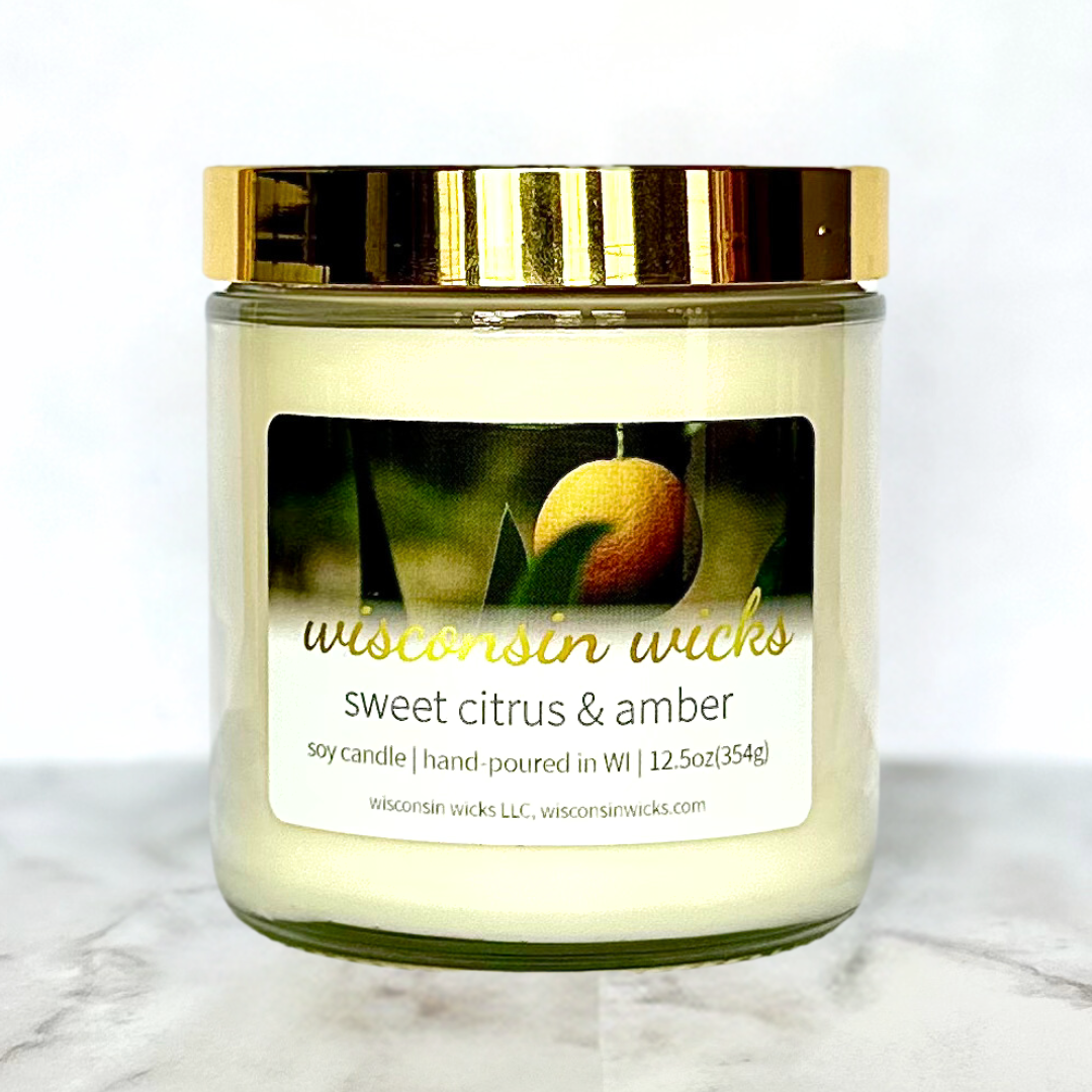 Aromatic candle labeled "Wisconsin Wicks Sweet Citrus & Amber" on a marbled surface.